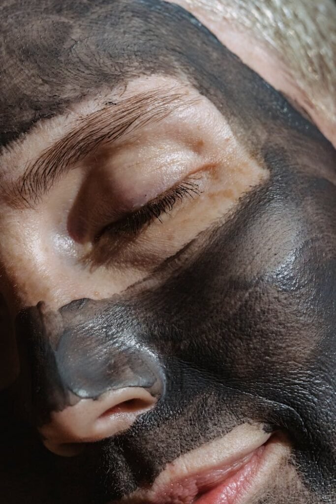 Crop face of relaxing blond lady closing eyes with clay mask on face during beauty procedure